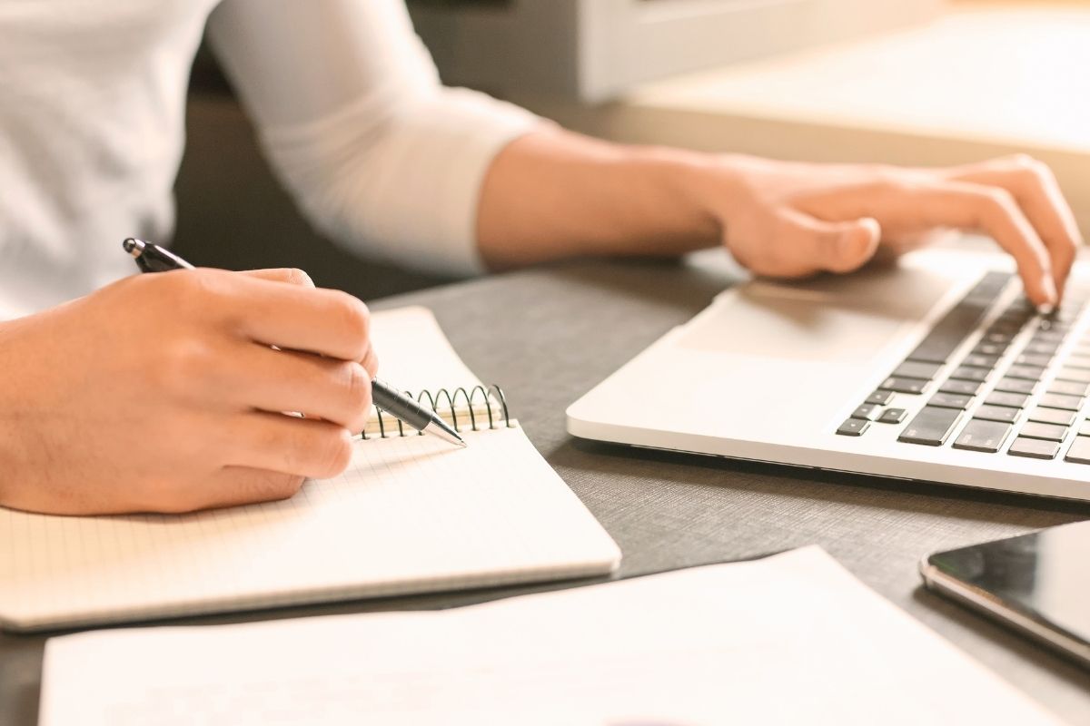 Student writing and using a laptop